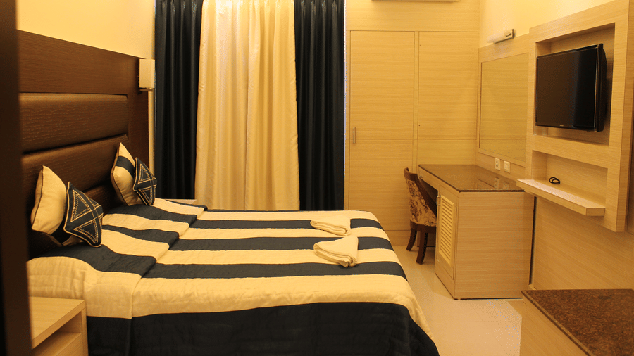 Interiors of the Deluxe Room at Hotel Shompen featuring a double bed, wall-mounted TV, and elegant blue and white curtains, ideal for travellers exploring the best Port Blair hotel deals.