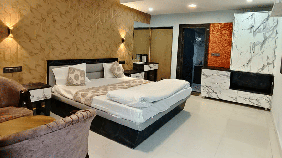 A modern bedroom with a large bed, patterned tan wall panelling behind the headboard, and dark wood furniture on a polished light-coloured floor | Nandan Resort