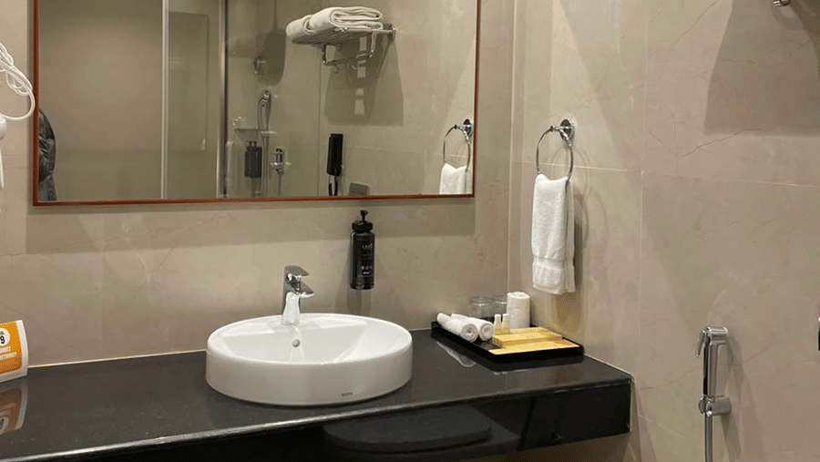 MM Legacy, Kanchipuram | A bathroom with a toilet seat, a sink, and other toileteries.