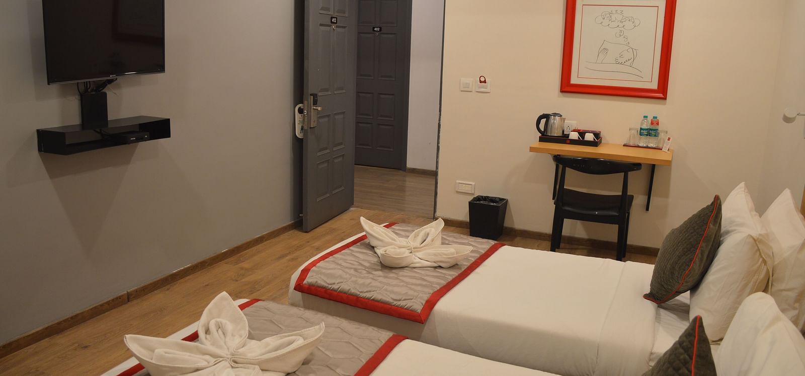 A bedroom featuring two single beds with a mounted television, and a framed artwork - Lords Eco Inn Belagavi