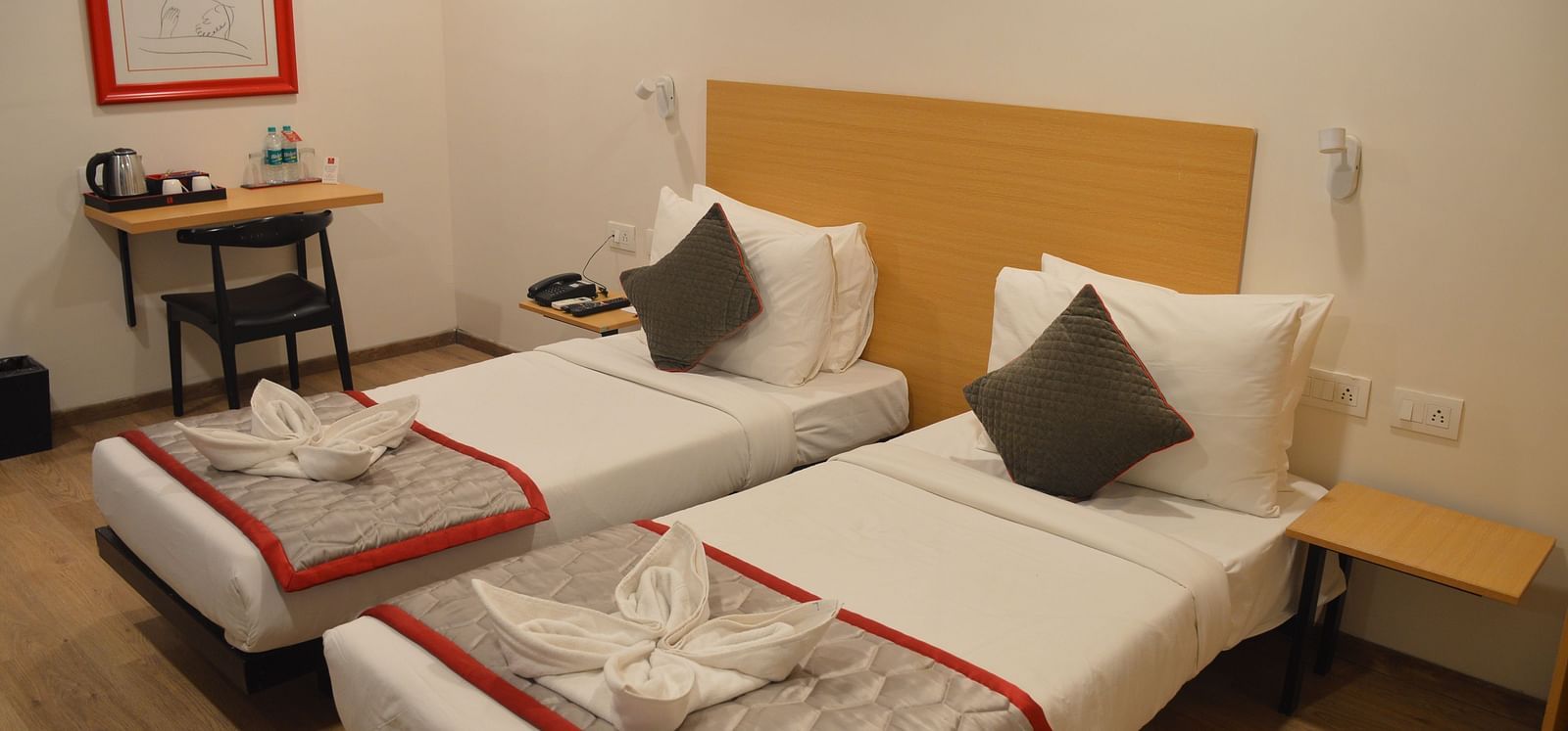 A bedroom featuring two single beds and a small work desk and chair in the corner - Lords Eco Inn Belagavi