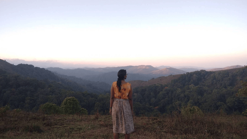 A person stands on a ridge looking at distant mountain ranges at dusk.