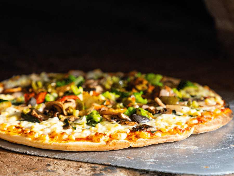 A loaded pizza in making, inside a big brick oven.