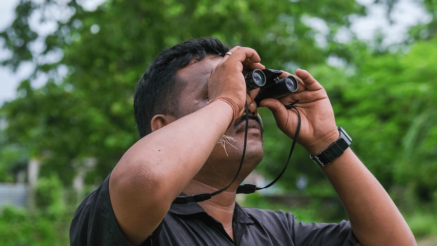 A man in a dark shirt looking through binoculars during a birdwatching session at Rhino & River Wildlife Retreat & Spa, Pobitora.