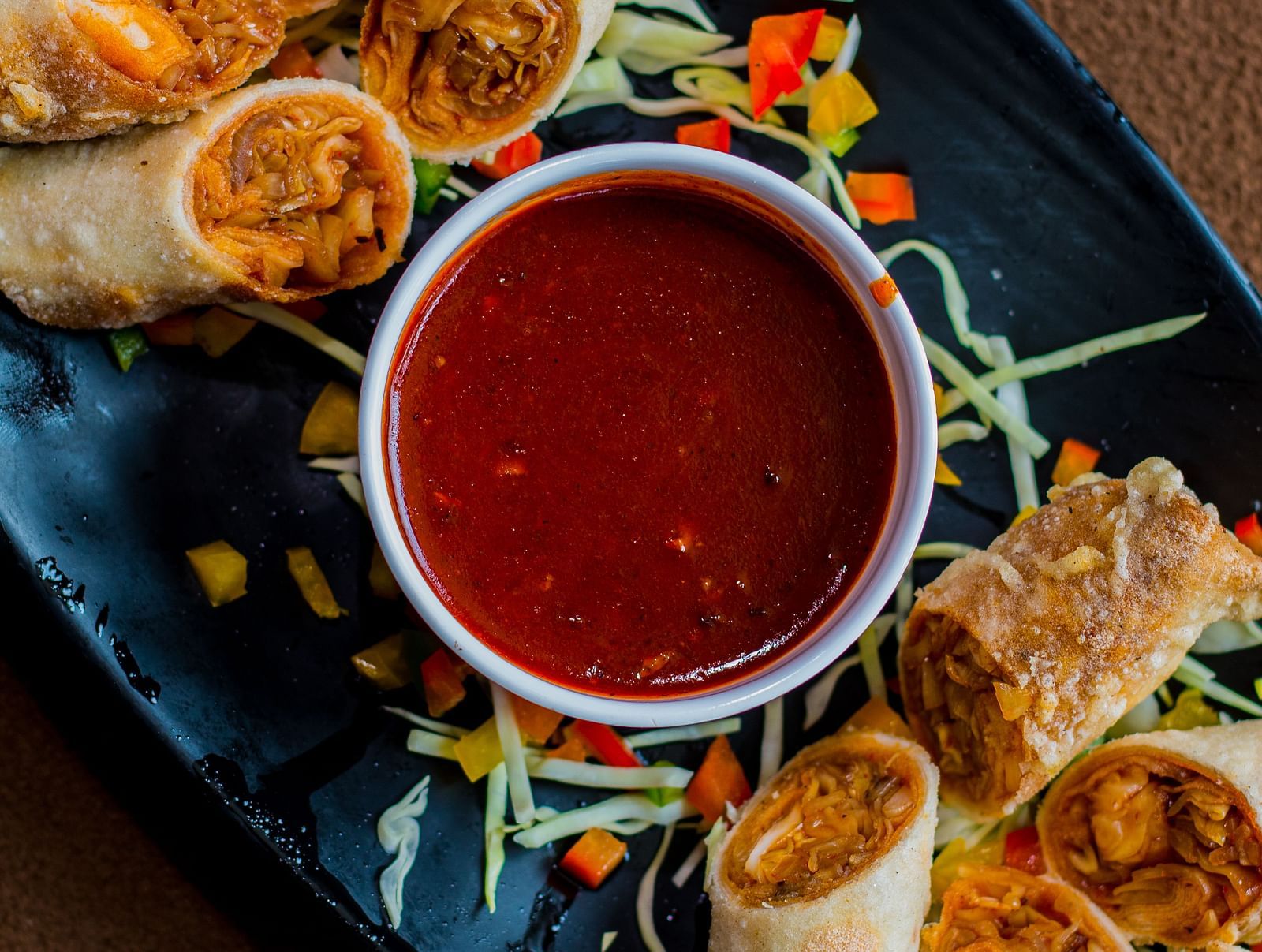 A serving of spring rolls arranged around a small bowl of dipping sauce.