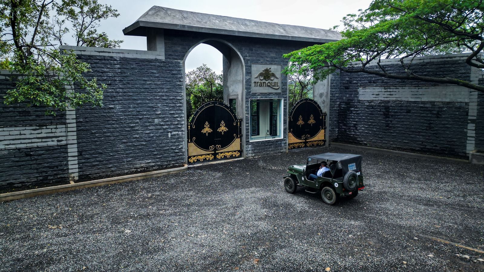 The front of a modern, grey stone building with a large gateway and a military jeep parked in the driveway - Tranquil Piedmont Estates & Resort, Lonavala