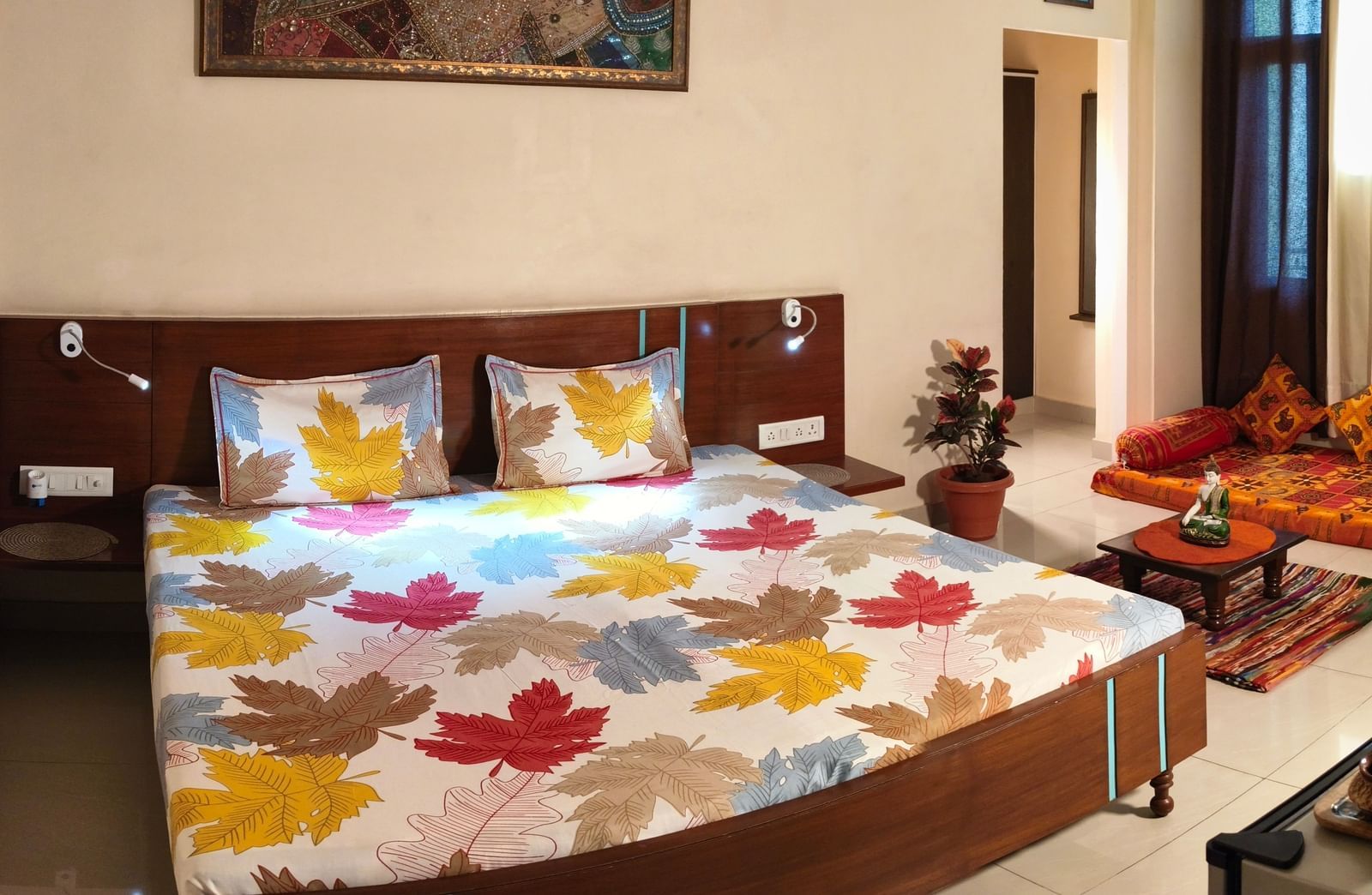 A spacious bedroom with a double bed, colourful bedding, a sofa set and a wall painting above the bed at Jaypore360 Homestay - Best Homestays in Jaipur.