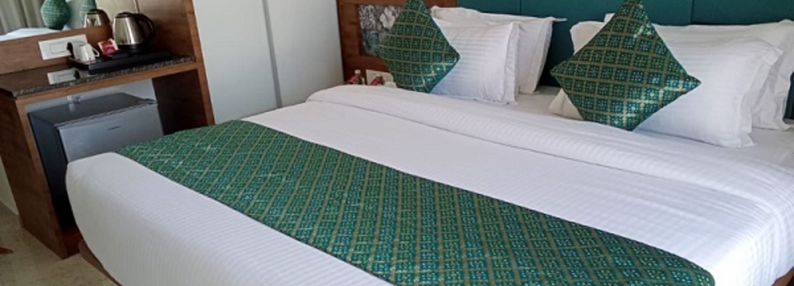 A room with a large bed which is neatly made with bedsheet, pillows and bedside tables at Angel Lords Eco Inn Amreli.