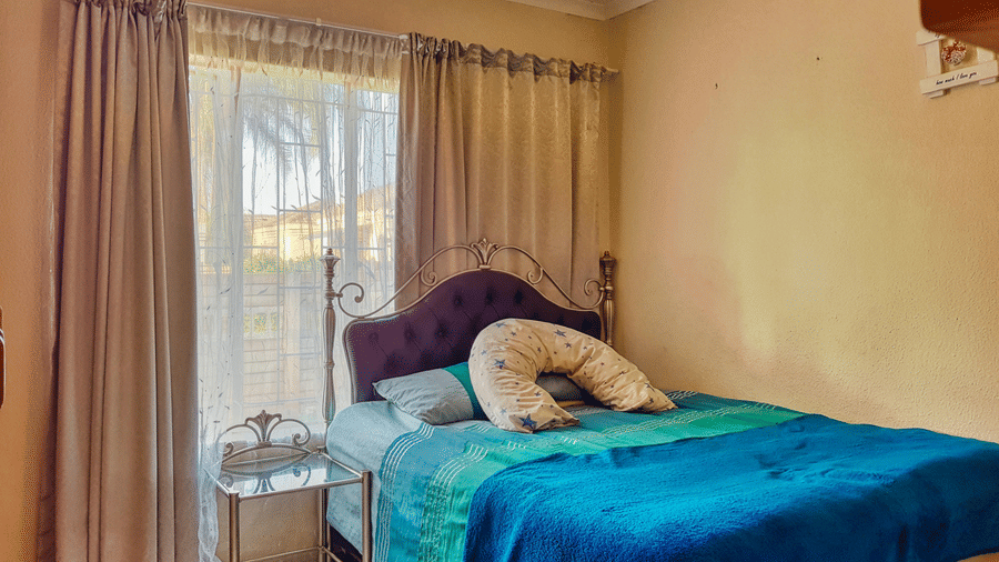 A bedroom featuring a double bed with blue sheets spread neatly over it with beige curtains covering the window behind it.