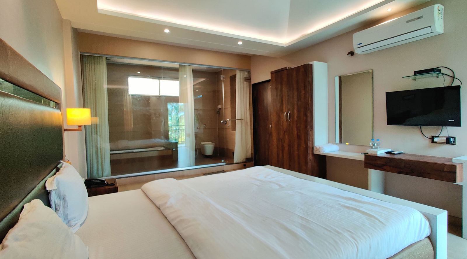 A Super Premium Room at The Kanila Resort with a queen sized bed, a nightstand, a TV, and a desk. 
