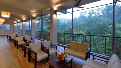 An open-air lounge or balcony with several wooden armchairs and small coffee tables overlooking a valley.