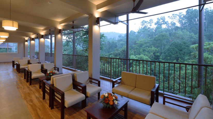An open-air lounge or balcony with several wooden armchairs and small coffee tables overlooking a valley.