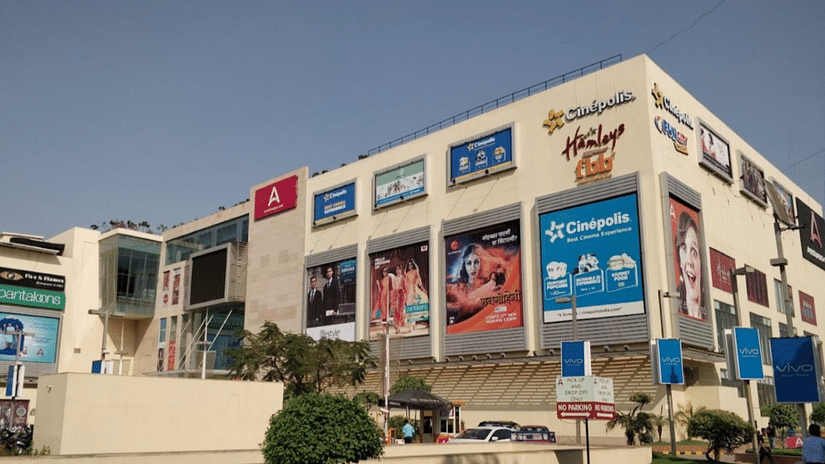 An exterior view of the Nexus Ahmedabad One building, prominently displaying large flyers advertising various brands, showcasing a vibrant shopping destination.