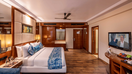 a king size bed room with a ceiling fan, wall-mounted TV, full length mirror, a dressing table, a wall attached cupboard, and centralised air-conditioning at Libra Lords Inn Jaipur