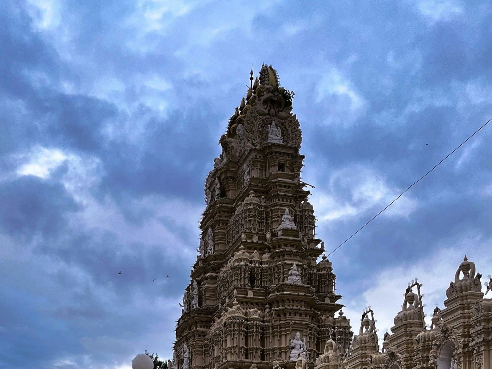 The side view of a large, pale-coloured temple tower with a red-tiled path leading away from the building.