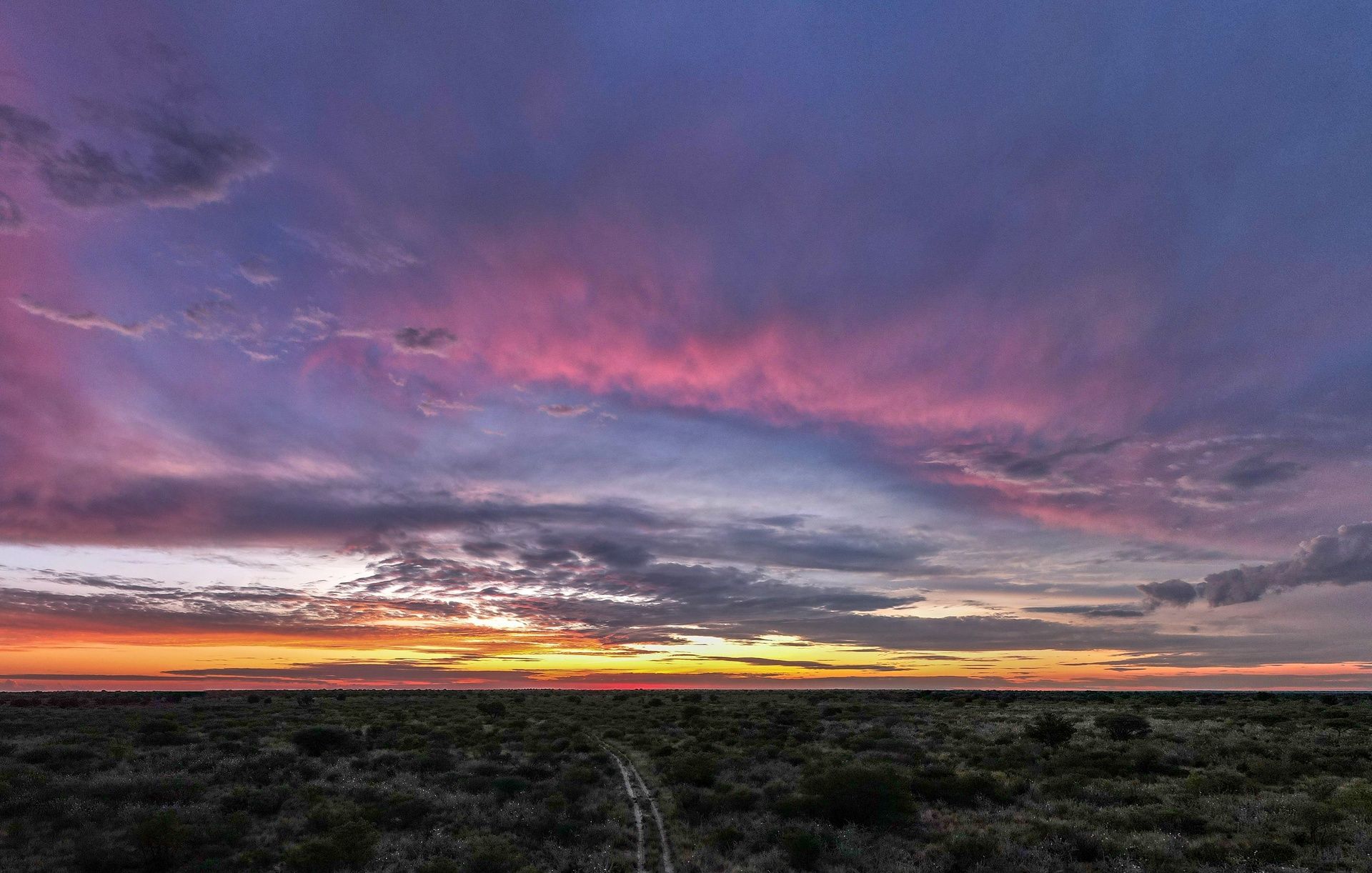 Vibrant sunset over a flat landscape with a dirt track.