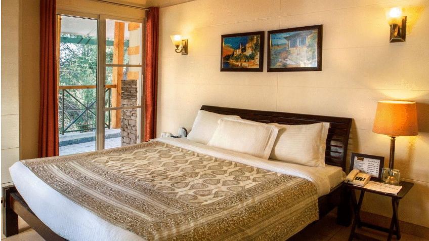 Deluxe room designed with aesthetic interior with  beautiful shades of brown while showcasing a beautiful balcony beside the bed - Lamrin Norwood Green, Palampur