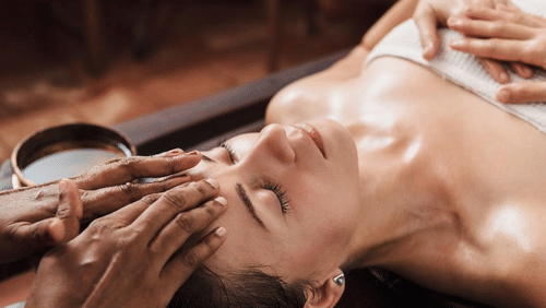 A person with closed eyes receives a head and face massage, with hands applying oil at YO1 Longevity & Health Resorts