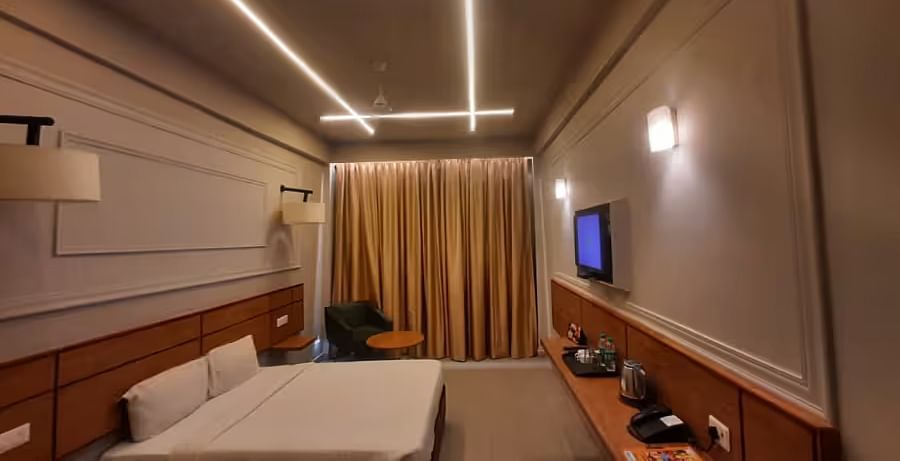 View of a modern hotel room with ambient lighting, a comfortable bed, and a wall-mounted TV - Max Hotel Prayagraj.