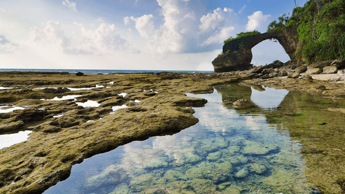 A natural coral bridge seen on Neil Island under a partially cloudy sky.