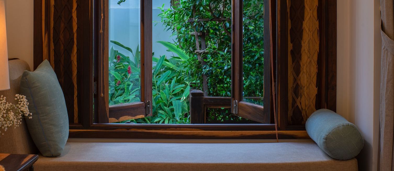 A comfortable sofa near a wooden window overlooking lush green trees - Alibu Resort Nha Trang