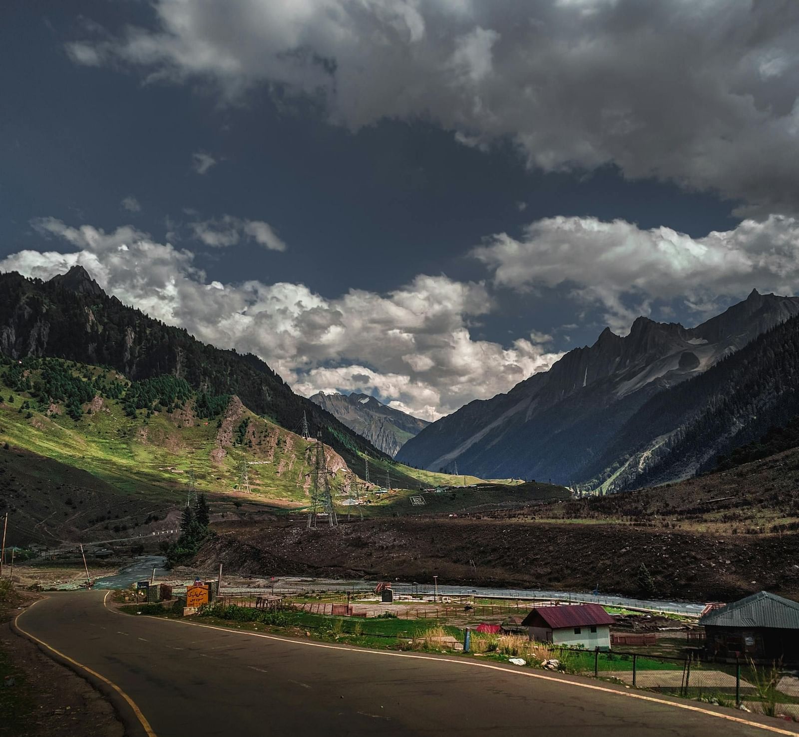 Curved road going through with mountains on both sides and clouds in the sky.