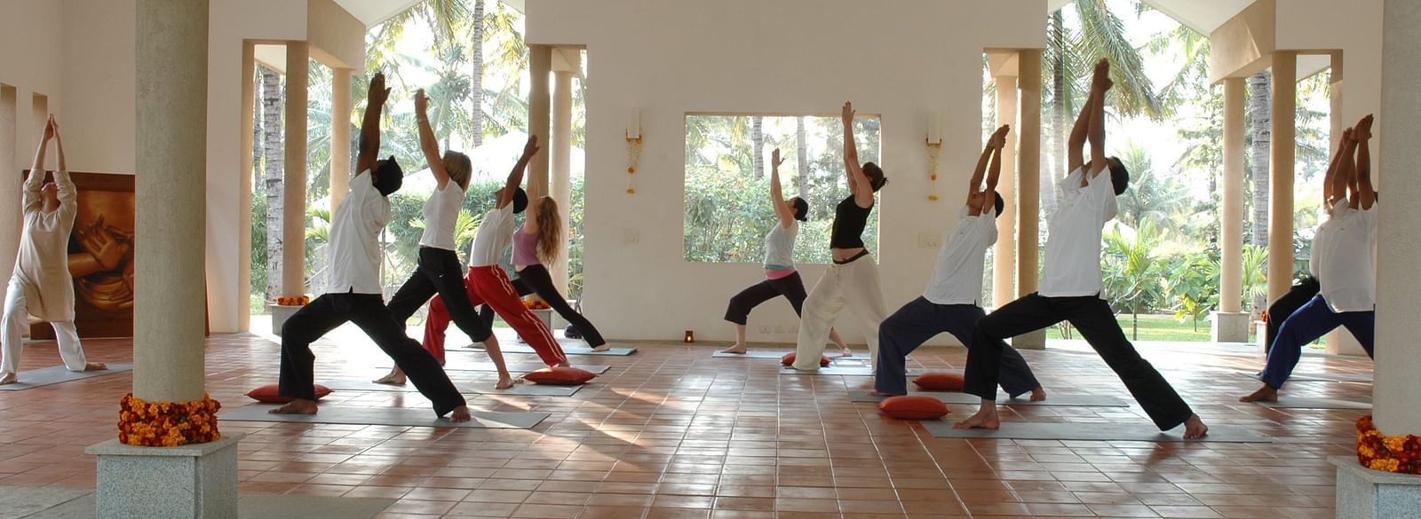 People doing yoga poses in a bright room, colorful rangoli on floor - Shreyas Retreat