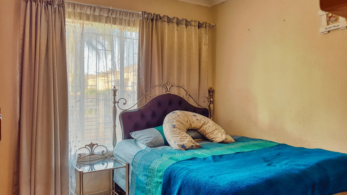 A bedroom featuring a double bed with blue sheets spread neatly over it with beige curtains covering the window behind it.