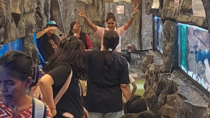 A vertical, brightly lit interior view of a crowded area at EsselWorld Fish Paradise, possibly a tunnel or hallway inside the aquarium, filled with many visitors.