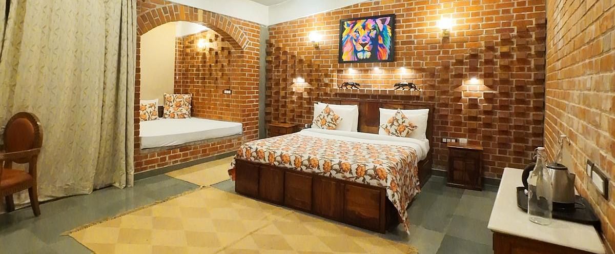 A bedroom at Tisya Farms, Gurgaon with a double bed, yellow-patterned floor mat, brick wall, and ceiling fan.
