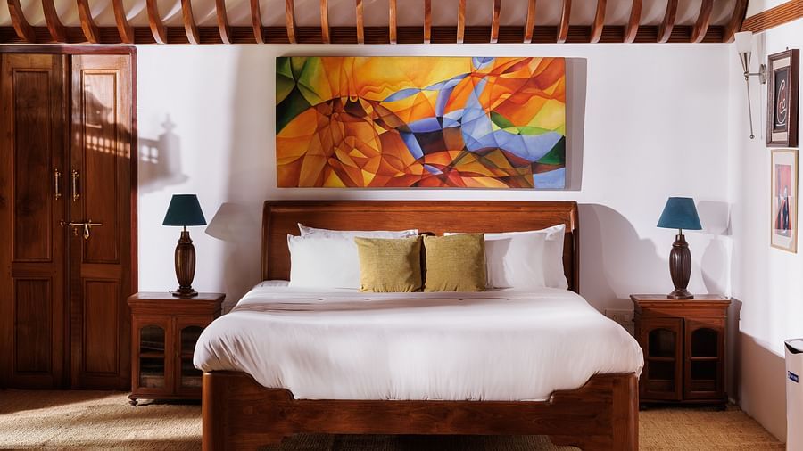 A close up shot of a bed, bedside tables, lamps and a painting hung on the wall at BluSalzz Villas - Muhamma Resort, Alleppey
