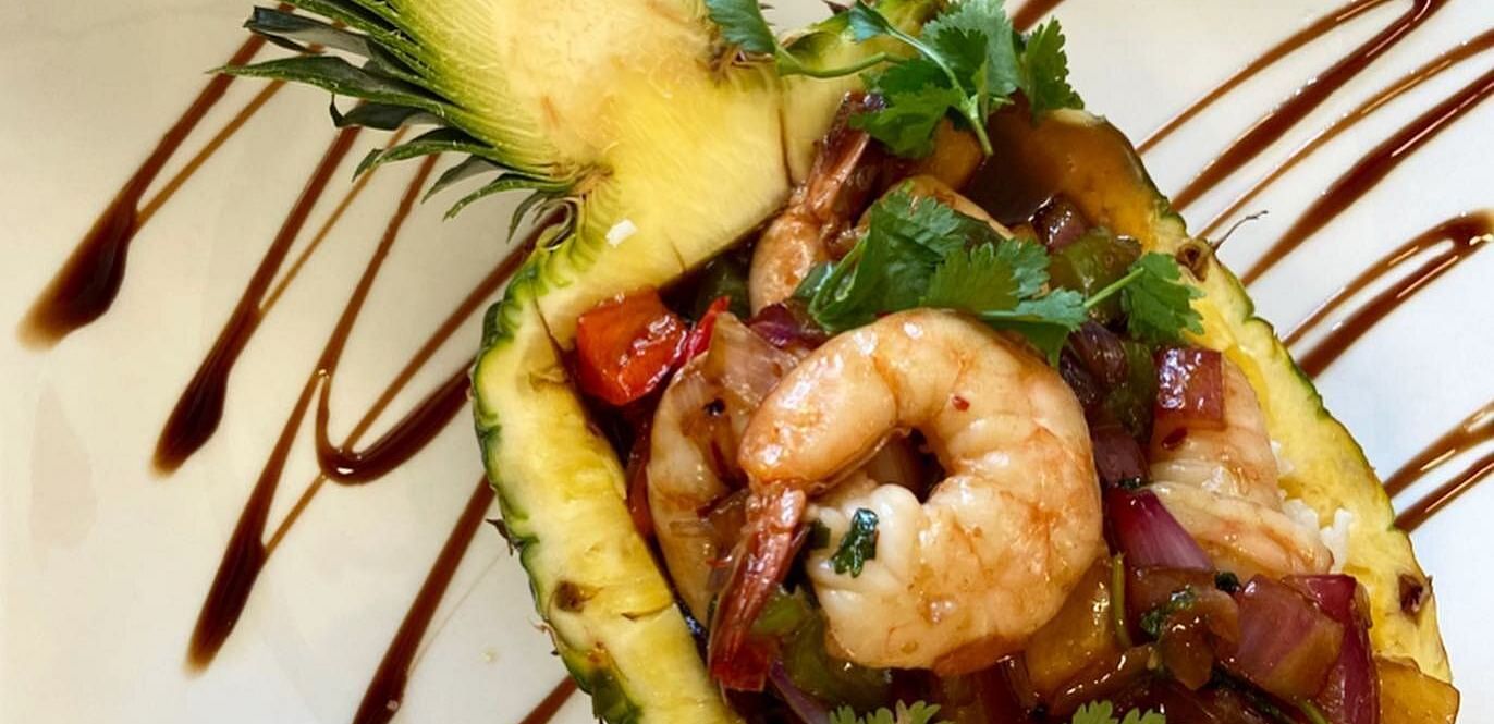 An image of prawn and vegetables served in pineapple on a plate garnished with ketchup
