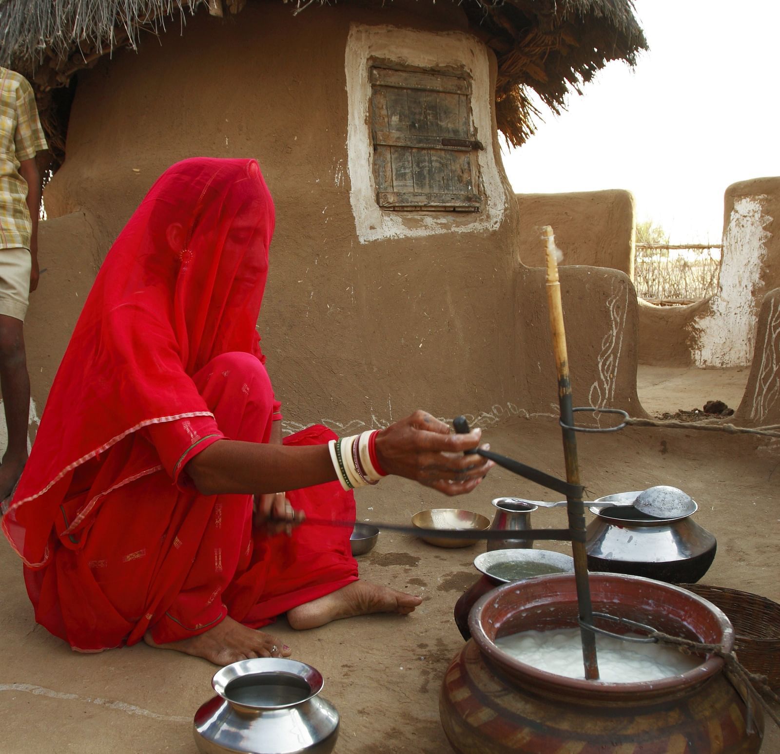 A lady cooking food in a village with her mud house next to her