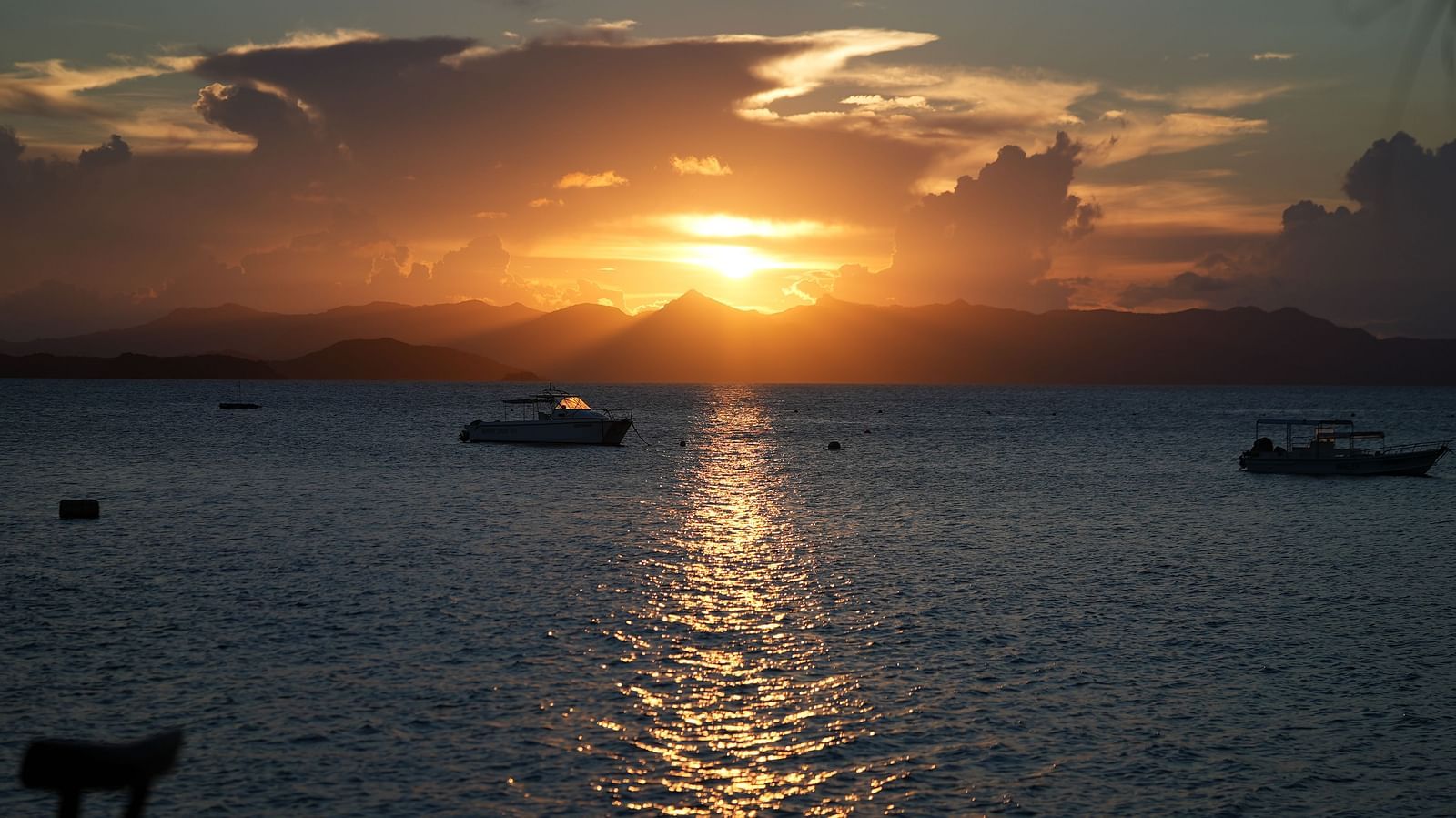 Sunset over the sea with boats on the water near Flower Island Resort.
