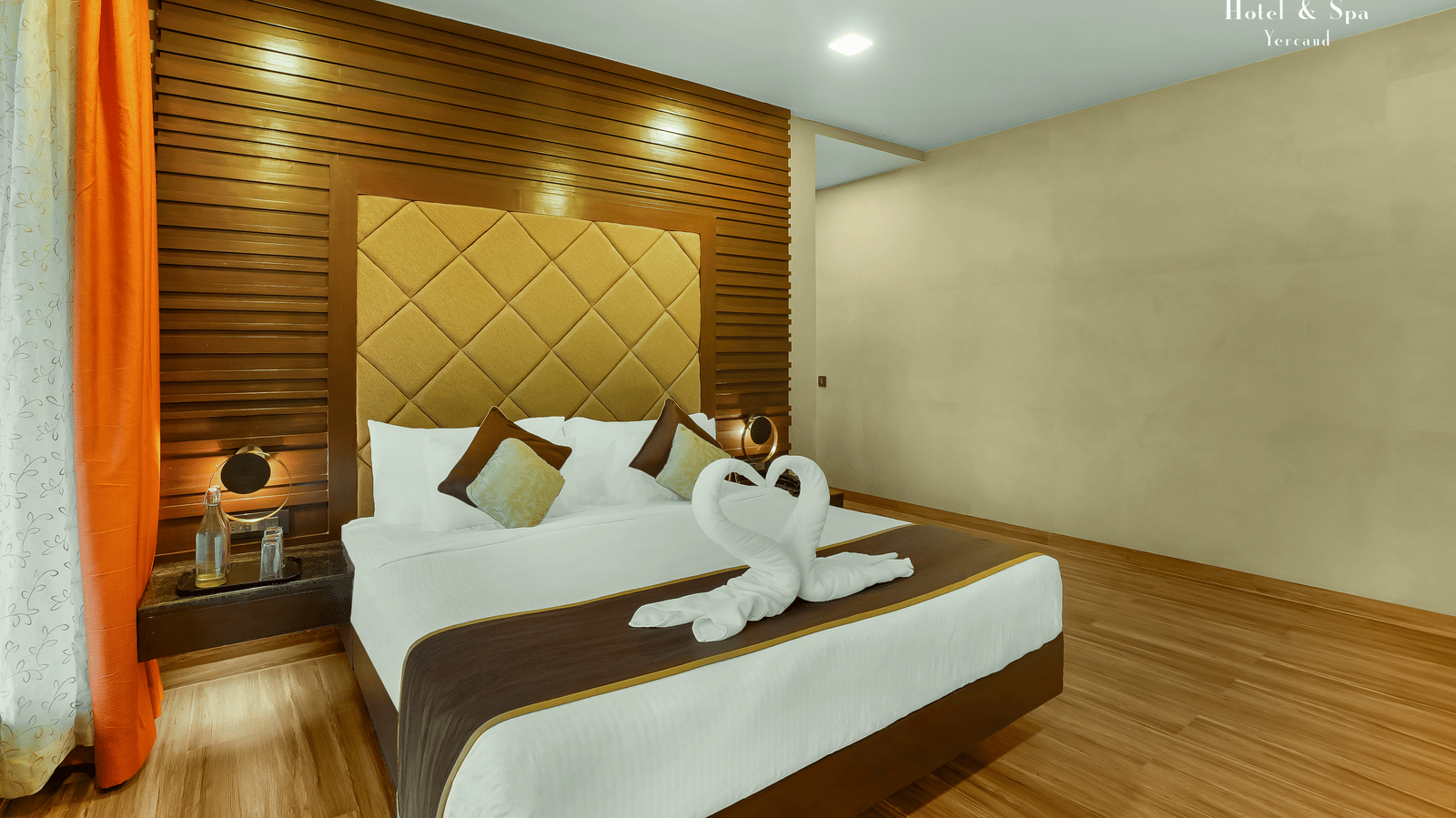 Artist Suite at Grand Palace, Yercaud with double bed, bedside tables, headboard, lighting and curtains, showing modern indoor accommodation.