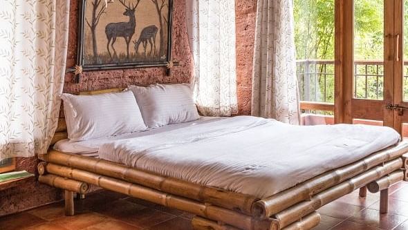 A bedroom with a wooden bed frame, tan walls, and a window with patterned curtains.