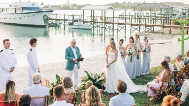 Ceremony attendees sit beside water and watch a wedding event, with a boat and dock in the background at Abaco Inn.