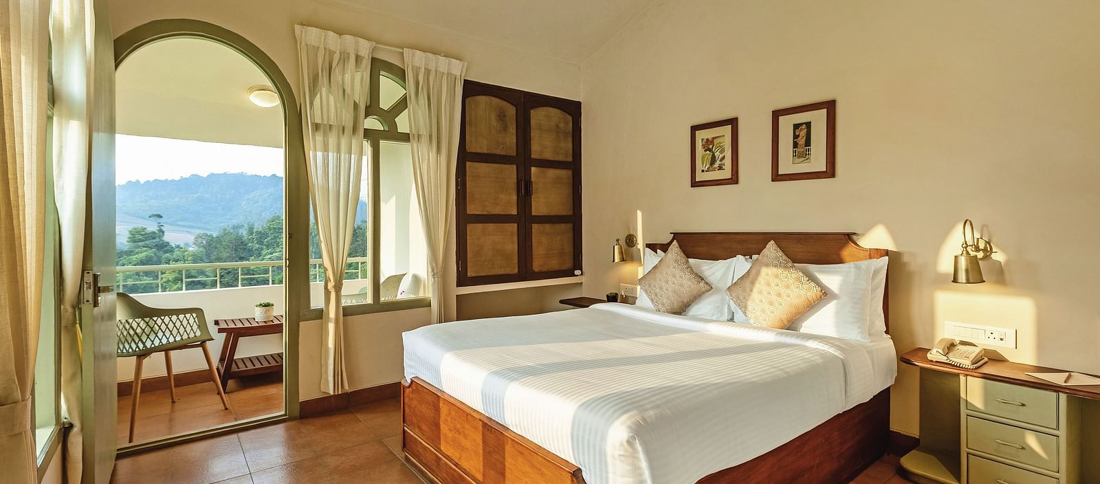 Bedroom at Mango Hill Shola, Ooty, with a double bed, wooden flooring, and an arched window offering an outdoor view.