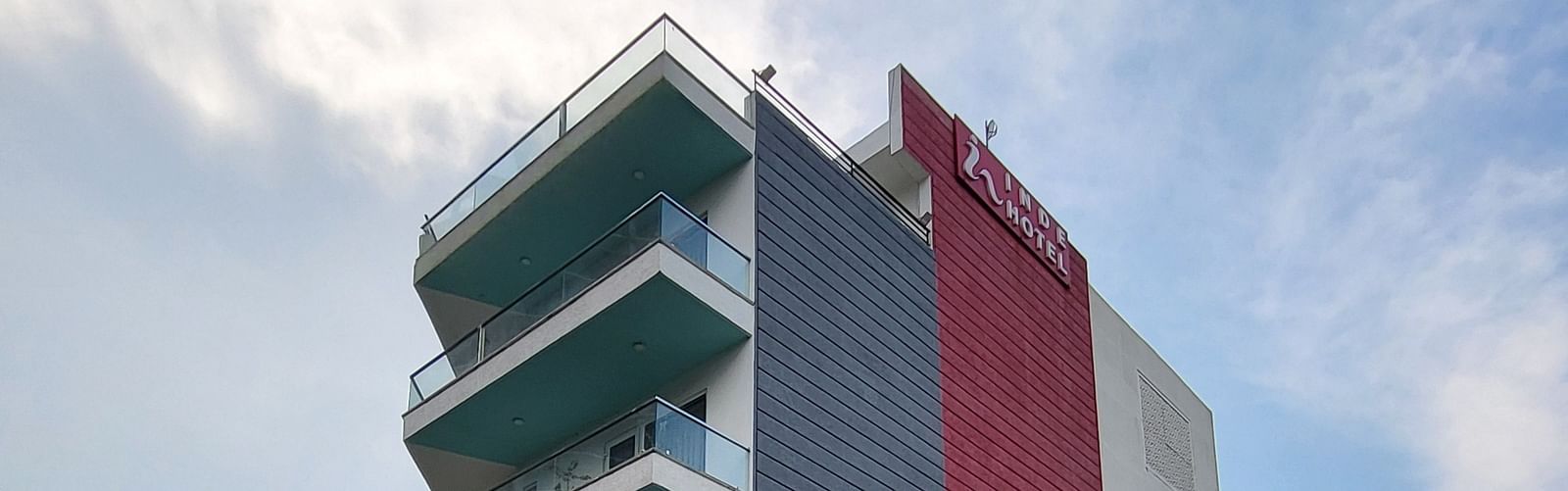 A facade of Inde Hotel Golf Course Extension featuring multiple storeys and balconies on each floor, and cars parked on the lawn