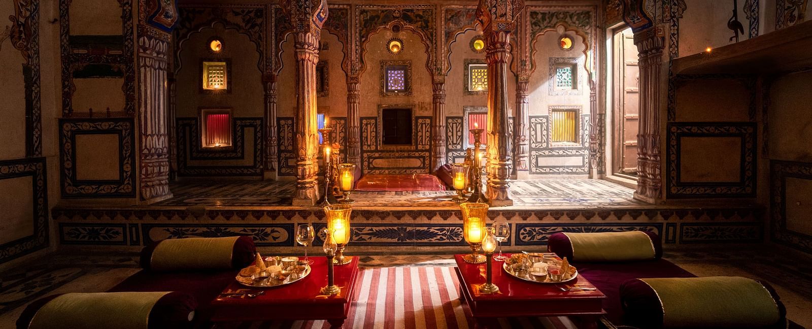 A richly decorated lounge at Fort Barli, featuring ornate arches, warm lighting, and plush seating, exudes a sense of historical grandeur and intimate ambience.