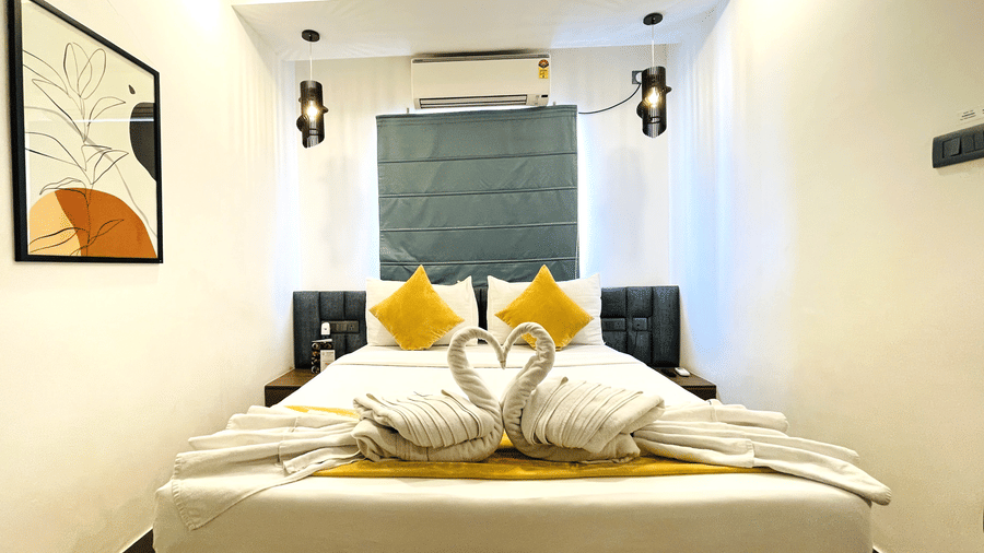 King bed at Hotel Kyzen Smart Stays Madhapur with yellow cushions, swan towel folding, teal headboard panel, framed artwork, and wall-mounted air conditioner above.