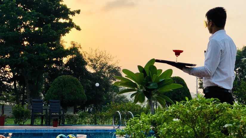 A waiter holding a drink, standing next to the swimming pool during the evening at VITS Kamats Resort, Silvassa.