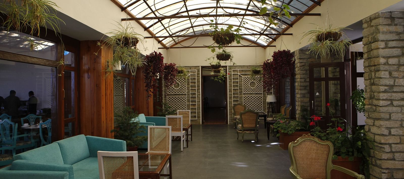 A close up shot of a lounge in Almora with a teal sofa, chairs, and a transparent ceiling from which potted plants are hung - BluSalzz Escapade - Anant Rasa Resort