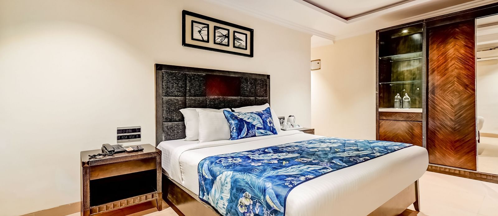 Deluxe room with a private balcony featuring a large bed, flanked by wooden bedside tables, and a photo frame mounted above the headboard