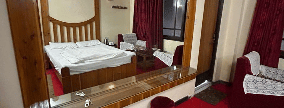 Hotel room featuring a bed with a wooden headboard, a large mirror, red carpet, and a striped rug at Hotel Dolphin Darjeeling.