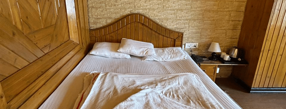 Close-up of a neatly made double bed with light bedding, wooden headboard, and wooden ceiling at Hotel Dolphin Darjeeling.