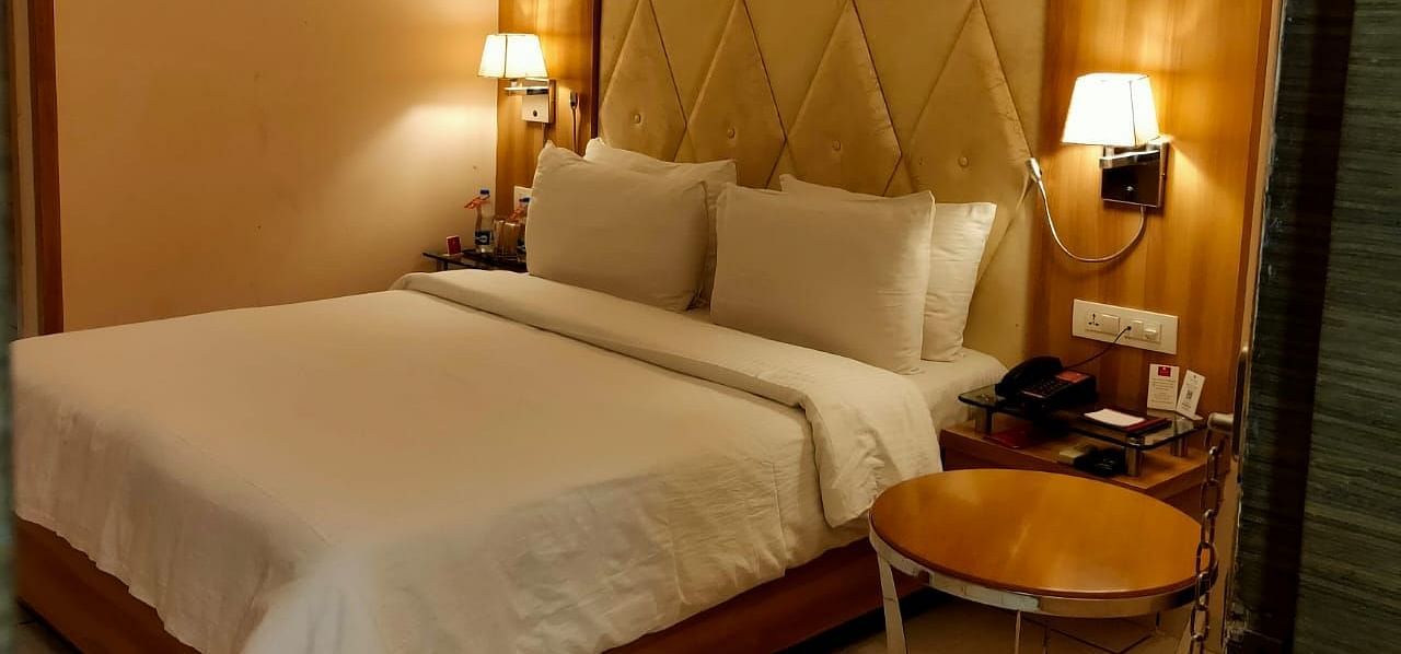 A cosy hotel bedroom  featuring a neatly made bed, bedside lamps, and a decorative headboard - Rang Lords Inn Bharuch