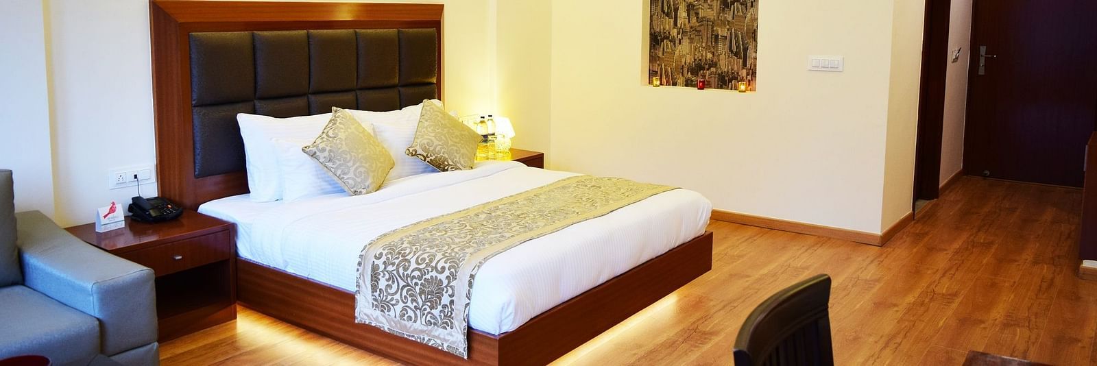 The image shows a hotel room with a large bed, two nightstands, and a couch in the background  | DLS Serenity Resort and Spa
