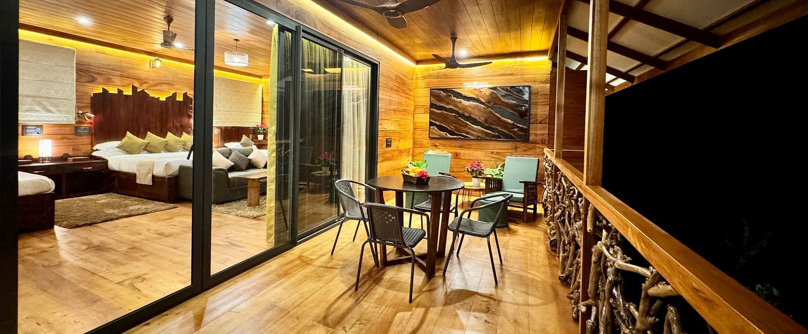 A tree house with large glass windows and a wooden balcony overlooking the surroundings at night - BluSalzz Collection - Tranquil Resort, Wayanad