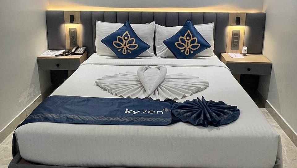 Bed with decorative cushions, side tables, and soft lighting, featuring towel art in the shape of a heart at Hotel Kyzen HiTech City – Your Zenly Stay